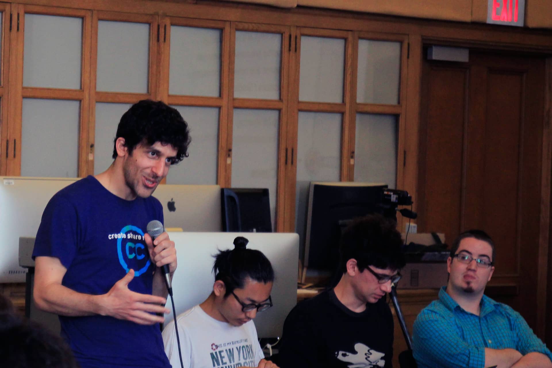 Man in a classroom with a microphone speaking out to a group of participants"