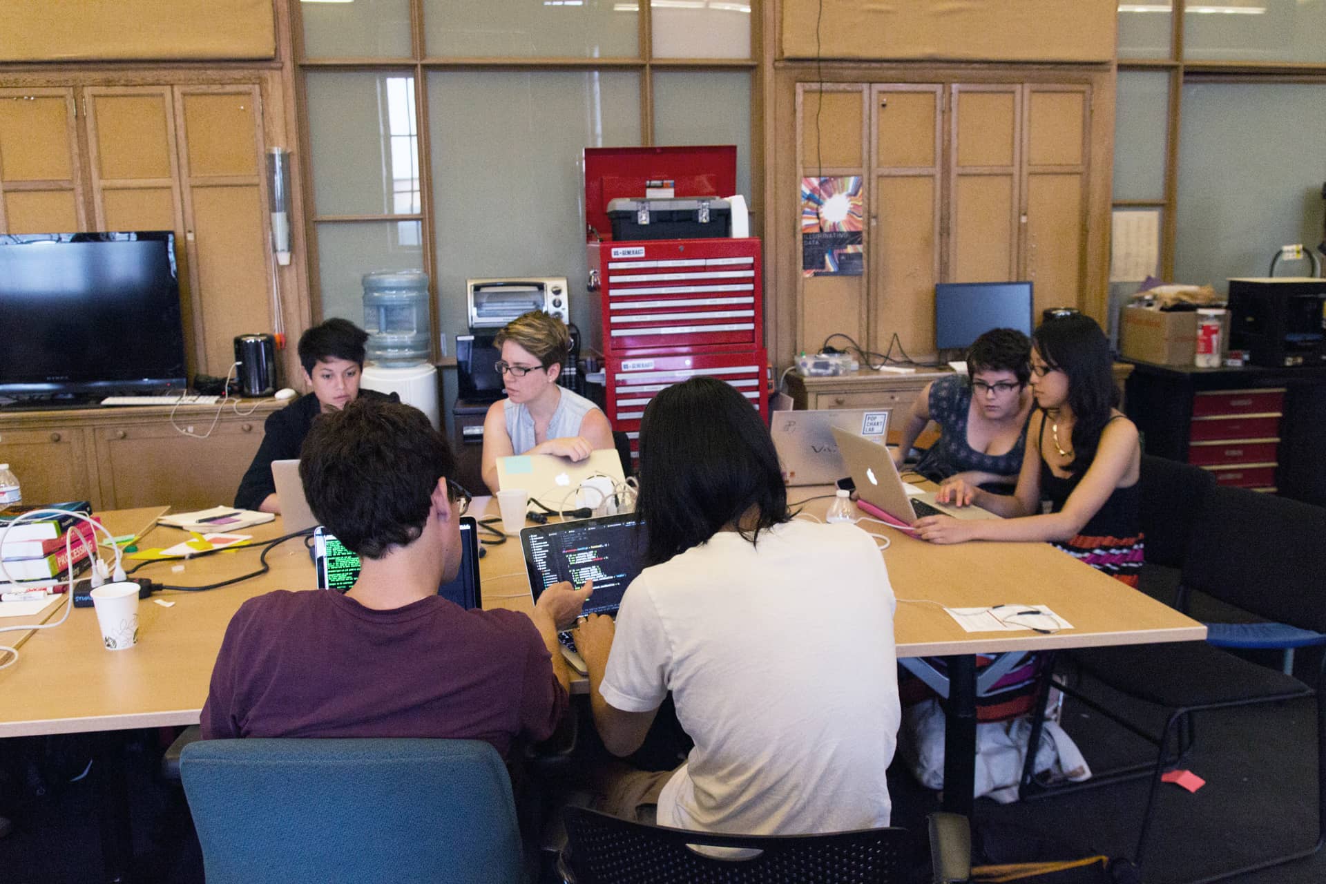 Participants sit around a table looking at each others laptops and compare code"